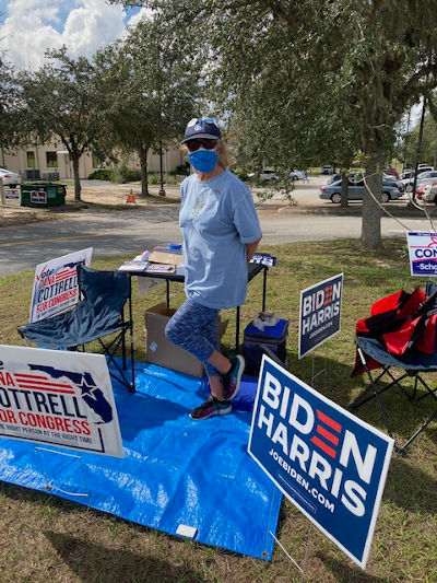 woman poll greeter in blue by table and signs